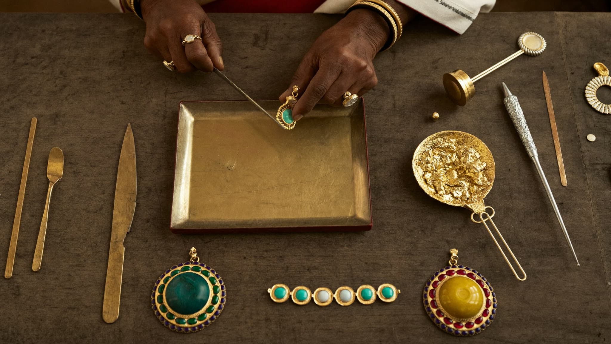 A jeweler's hands setting polki stones into gold kundan at a workbench